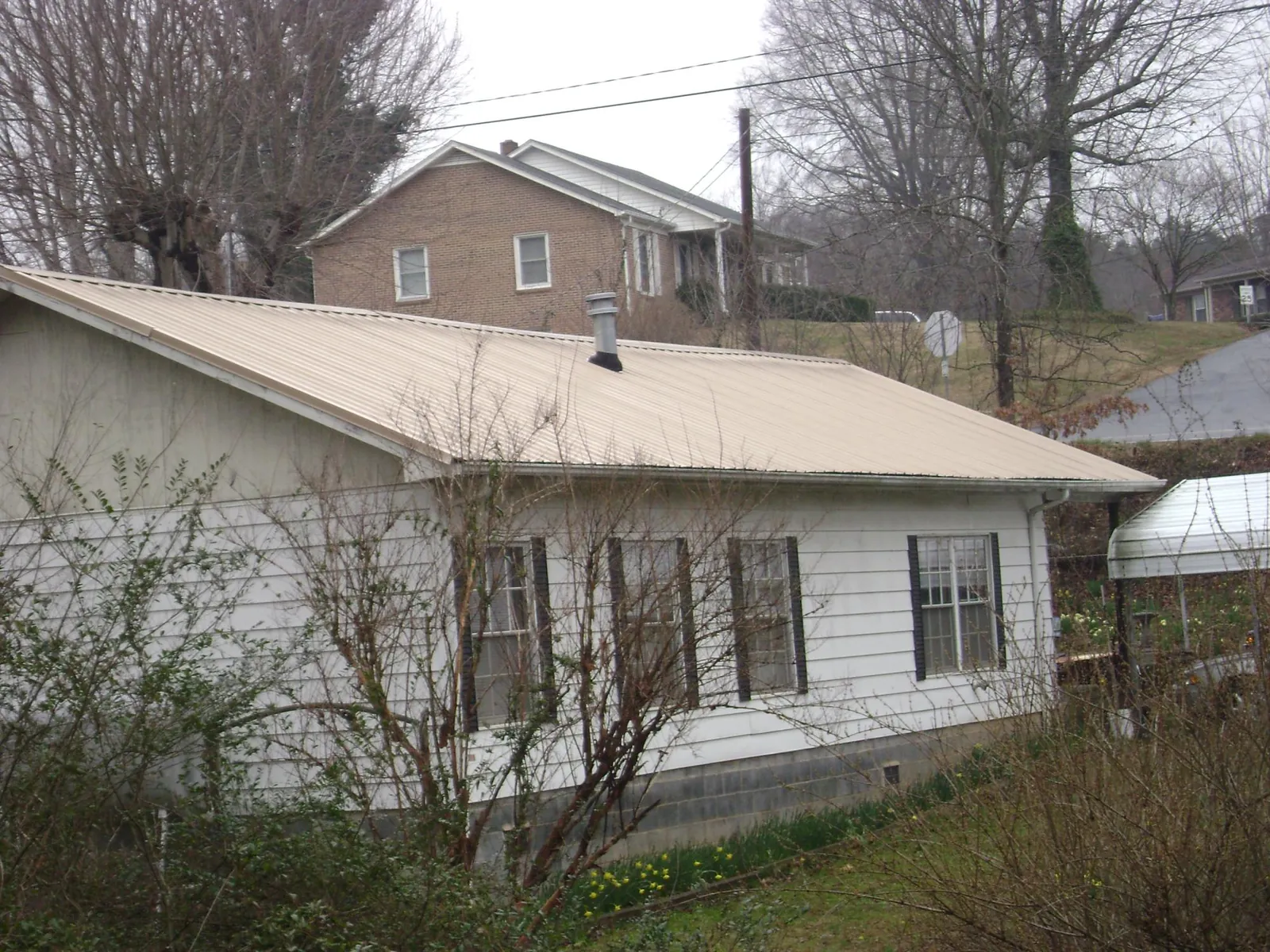 Tan metal roof on a white sided house set into a hillside — Commercial Roofing by Roofing Brothers in Sparta